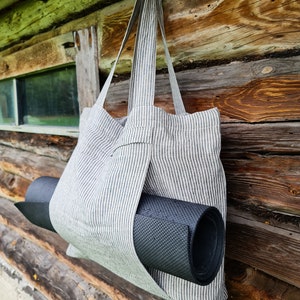 May include: A striped tote bag made of linen with a black yoga mat tucked inside. The bag is hanging on a wooden wall.