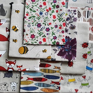 Puede incluir: Una colección de cuadrados de tela con varios patrones, incluyendo abejas, zorros, ovejas, peces y flores. Las telas son todas de un material similar al lino y tienen un aspecto rústico y hecho a mano.