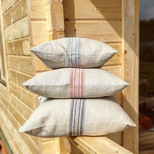 May include: Three linen pillows stacked on top of each other. The top pillow has blue and white stripes, the middle pillow has red and white stripes, and the bottom pillow has black and white stripes.