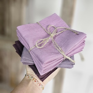 Peut inclure: Une pile de serviettes en lin pliées dans des tons de violet, du prune foncé au lavande clair. Les serviettes sont attachées avec de la ficelle, créant une présentation rustique et élégante. Idéal pour la décoration intérieure ou les événements.