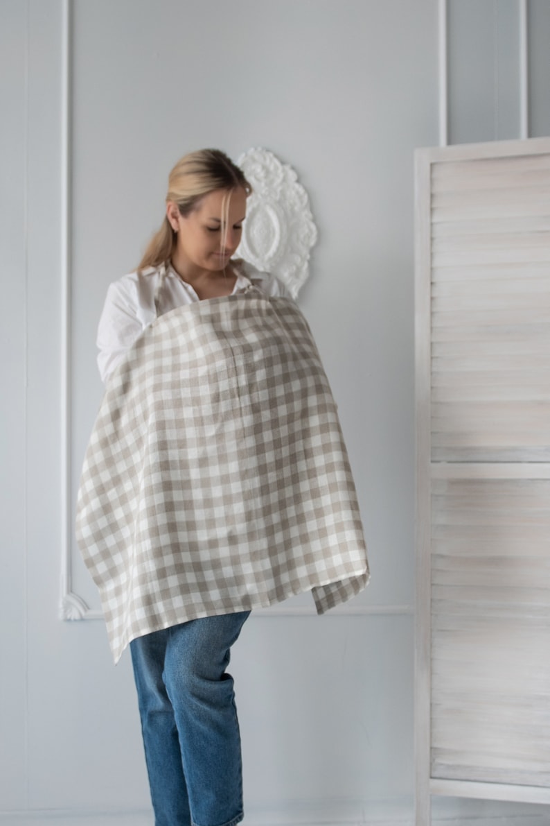 Pu&ograve; includere: Una donna con una camicia bianca e jeans blu sta usando un copriallattamento a quadri beige e bianchi.