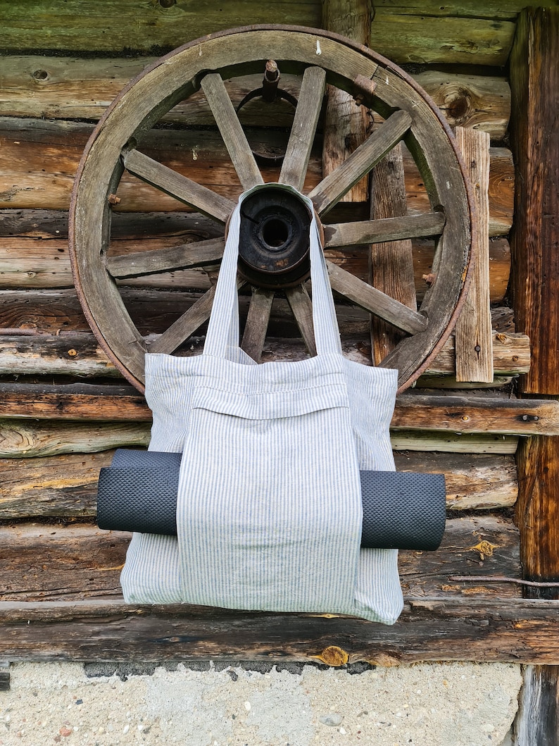 May include: A white and blue striped tote bag with a black yoga mat inside. The bag is hanging from an old wooden wagon wheel.