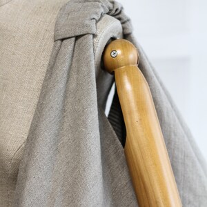May include: A close-up of a gray linen fabric draped over a wooden dress form. The fabric is gathered at the shoulder and the form's arm is visible.
