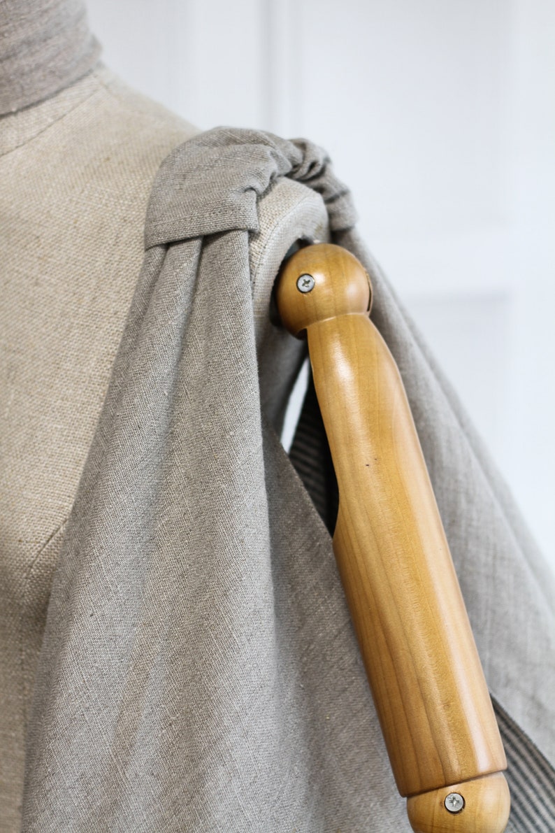 May include: A close-up of a gray linen fabric draped over a wooden dress form. The fabric is gathered at the shoulder and the form's arm is visible.