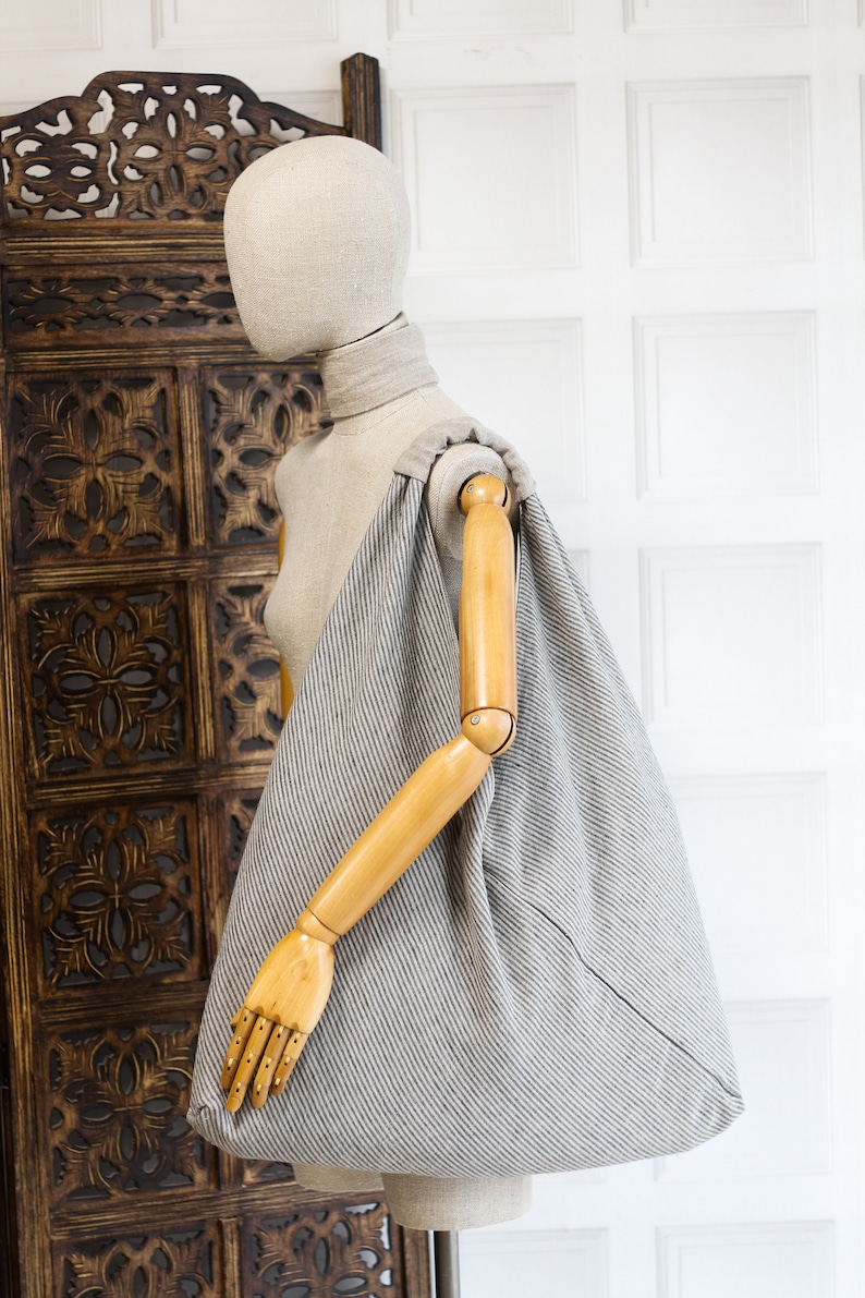 May include: A gray and white striped linen tote bag with a wooden handle. The bag is large and roomy, and it is perfect for carrying everyday essentials.