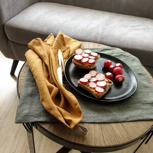 Puede incluir: Dos s&aacute;ndwiches abiertos con rodajas de r&aacute;bano encima, servidos en un plato negro con un acompa&ntilde;amiento de r&aacute;banos rojos. El plato est&aacute; sobre una mesa de madera con una servilleta de lino gris y amarillo mostaza.