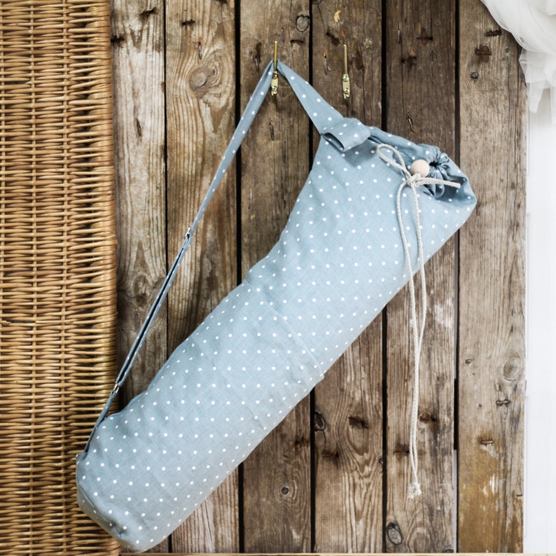 May include: A light blue yoga mat bag with white polka dots and a drawstring closure. The bag has a long strap for carrying over the shoulder.