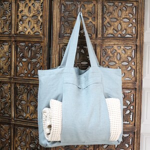 May include: A light blue tote bag made of linen with a white waffle weave towel inside. The bag is hanging on a wooden screen with intricate carvings.