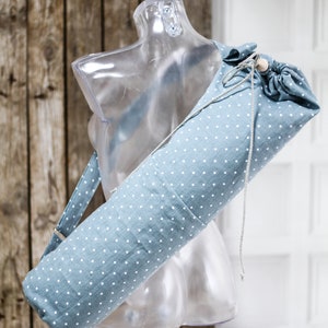 May include: A blue yoga mat bag with white polka dots and a drawstring closure. The bag has a long strap for carrying over the shoulder.