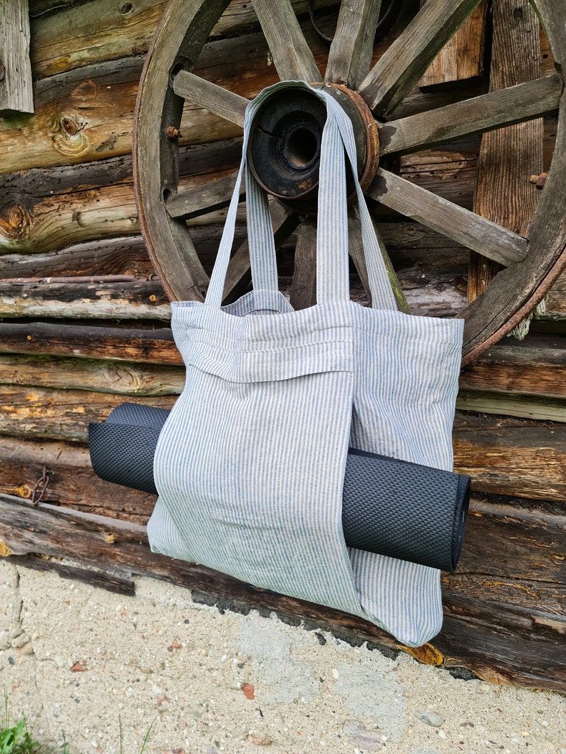 May include: A striped tote bag made of linen with a black yoga mat tucked inside. The bag is hanging on a wooden wheel.