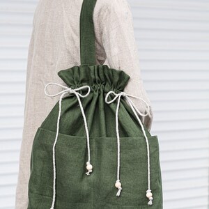 May include: A large, green canvas tote bag with a drawstring closure and two side pockets. The bag has a long strap and is decorated with wooden beads.