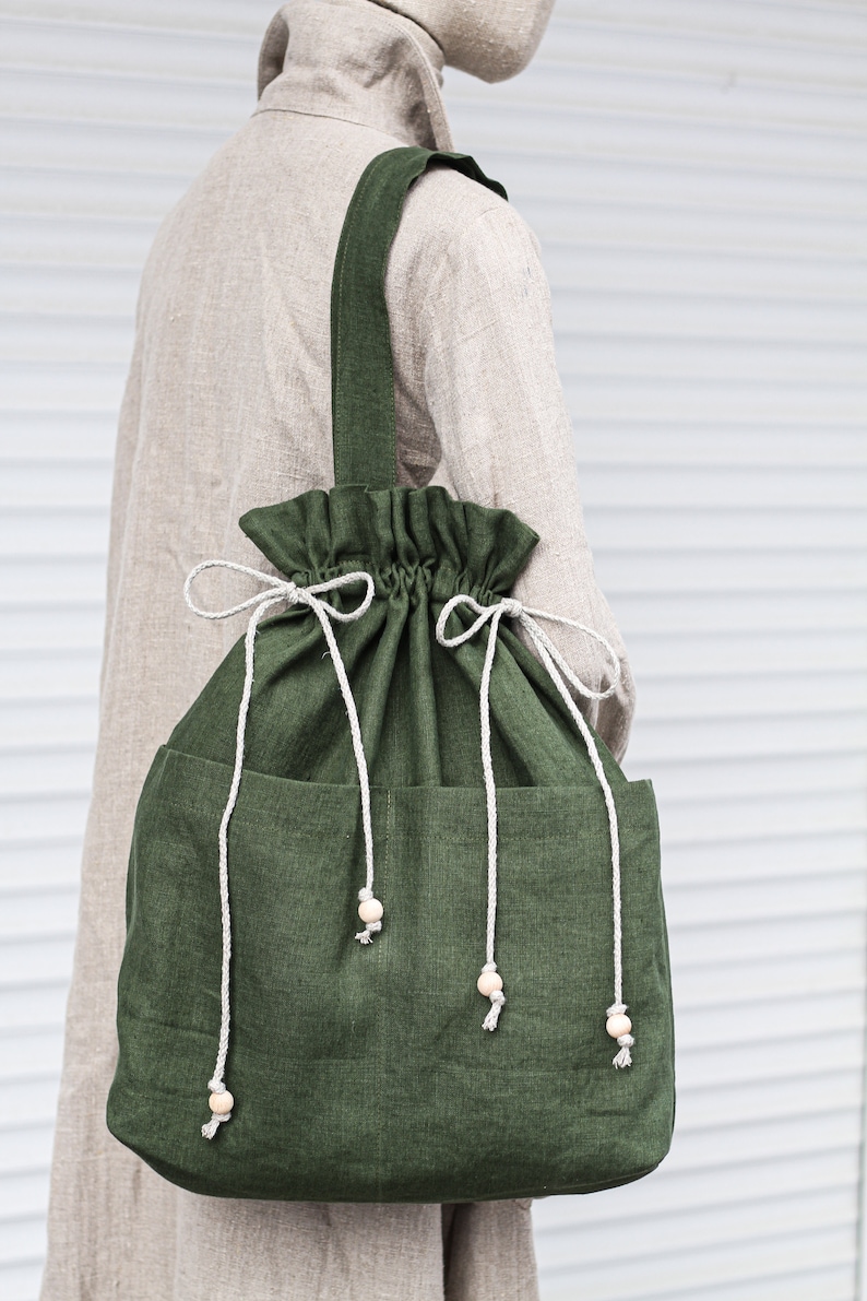 May include: A large, green canvas tote bag with a drawstring closure and two side pockets. The bag has a long strap and is decorated with wooden beads.