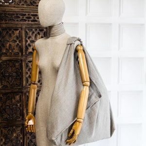 May include: A gray linen tote bag with a wooden handle, displayed on a mannequin with a wooden arm.