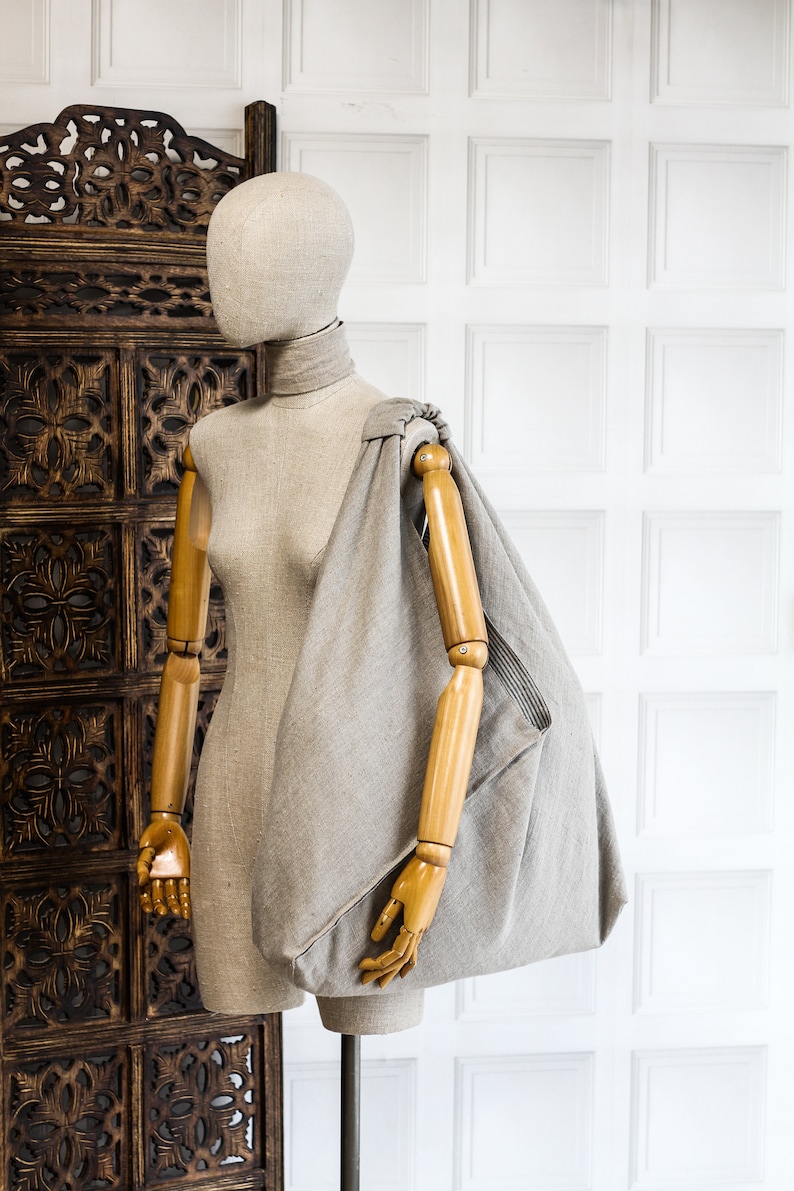 May include: A gray linen tote bag with a wooden handle, displayed on a mannequin with a wooden arm.