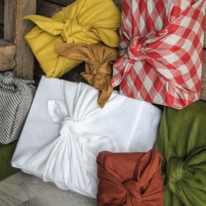 May include: Five fabric-wrapped gifts in various colors and patterns. The gifts are wrapped in yellow, red and white gingham, white, brown, and green fabric.