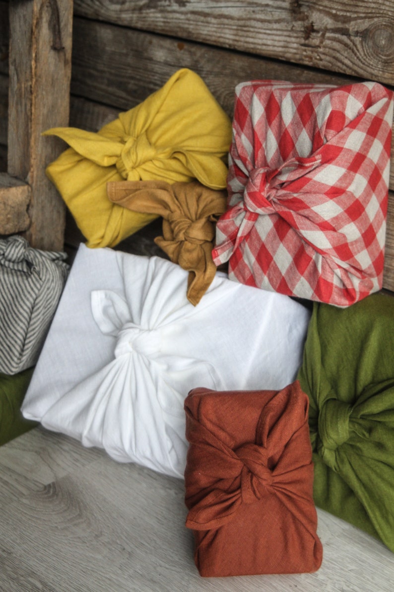 May include: Five fabric-wrapped gifts in various colors and patterns. The gifts are wrapped in yellow, red and white gingham, white, brown, and green fabric.