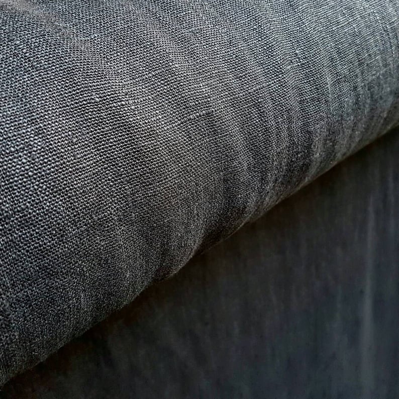 May include: Close-up of a dark gray fabric with a textured weave. The fabric is folded over itself, creating a layered effect.