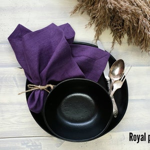 May include: A black dinner plate with a black bowl on top, a purple linen napkin tied with twine, and silver cutlery. The text "Royal purple" is in the bottom right corner of the image.