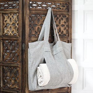 May include: A gray and white striped tote bag with a white towel inside, hanging on a wooden screen.