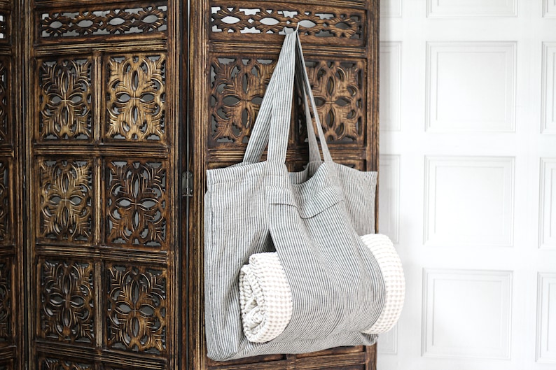 May include: A gray and white striped tote bag with a white towel inside, hanging on a wooden screen.