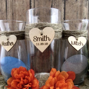 May include: Three clear glass vases with burlap ribbon and wooden heart tags. The tags are personalized with the names "Heather", "Smith 11.29.18", and "Mitch".