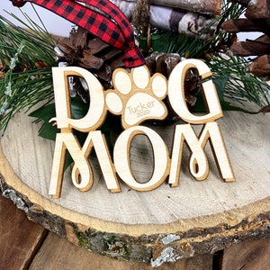 May include: Wooden Christmas ornament with the words "Dog Mom" and a paw print with the name "Tucker" and the year "2020" inside the paw print.