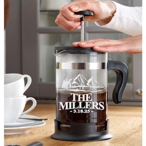 May include: A black and glass French press coffee maker with a mountain scene and the text "The Millers - 3.18.25 -" etched on the side.
