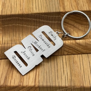 May include: A personalized silver-colored metal keychain with the names Brianna, Jacob, Olivia, Michael, Samantha, and Emily engraved on it. The keychain has a large, round key ring attached.