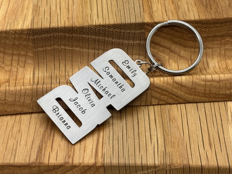May include: A personalized silver-colored metal keychain with the names Brianna, Jacob, Olivia, Michael, Samantha, and Emily engraved on it. The keychain has a large, round key ring attached.