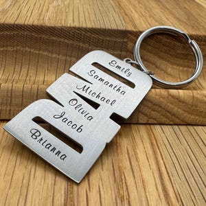 May include: A silver-colored metal keychain with the letter "B" cut out, featuring the names "Emily", "Samantha", "Michael", "Olivia", "Jacob", and "Brianna" engraved on it. The keychain has a silver ring attached.