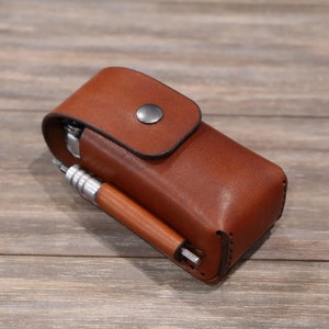 May include: A brown leather case with a snap closure and a silver button. The case is designed to hold a multi-tool and a pen.