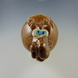 May include: A brown ceramic piggy bank with blue eyes and a textured surface. The piggy bank has a curly mane and a snout.