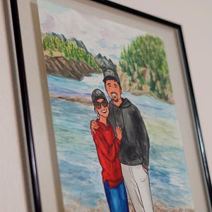 May include: A watercolor painting of a couple standing in front of a body of water. The man is wearing a black jacket and a baseball cap. The woman is wearing a red sweater and sunglasses. The background is a watercolor painting of a forest and a river.