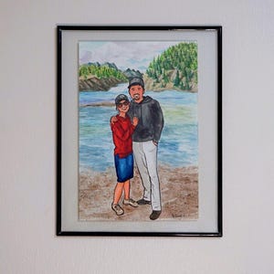 May include: A watercolor painting of a couple standing on a beach. The man is wearing a black jacket and a baseball cap. The woman is wearing a red shirt and blue jeans. The background is a watercolor painting of a lake and trees.