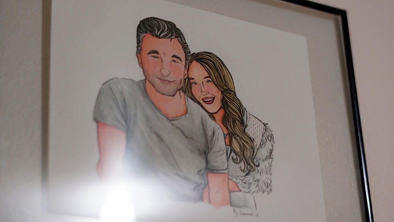 May include: A framed illustration of a couple. The man is wearing a gray shirt and the woman is wearing a white fur coat. They are both smiling.