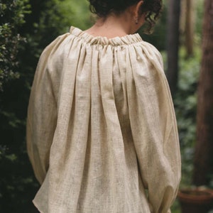 Pode incluir: Uma blusa de linho cor creme com decote franzido e mangas compridas. A blusa &eacute; feita de um tecido leve e respir&aacute;vel e tem um caimento solto.