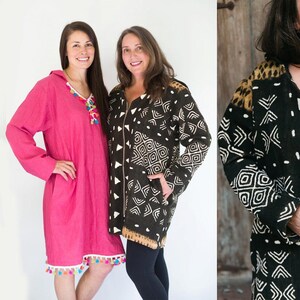 May include: Three hooded robes in the image. Two are solid colors, one is a vibrant pink with colorful tassel trim, and the other is a black and white patterned robe with a leopard print shoulder detail. All have long sleeves and pockets.