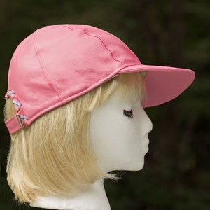 May include: A pink leather baseball cap with a white and blue braided strap. The cap is on a mannequin head with blonde hair.