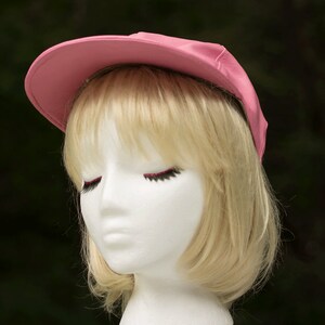 May include: A pink baseball cap with a black brim. The cap is on a white mannequin head with blonde hair.