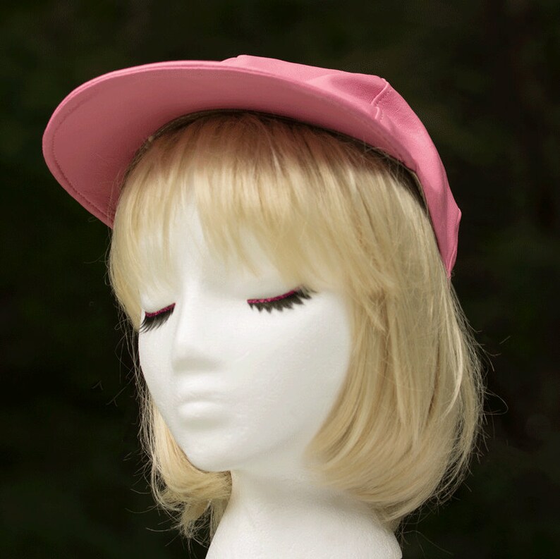May include: A pink baseball cap with a black brim. The cap is on a white mannequin head with blonde hair.
