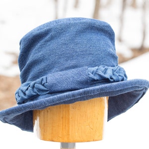 Blue denim hat with upturned curled brim and optional braided hatband. Sewn from your choice of denim fabric in 3 colors--Medium-dark blue, indigo blue, indigo blue with lacy or small snowflake motif. Its tall crown & soft folds has full coverage.