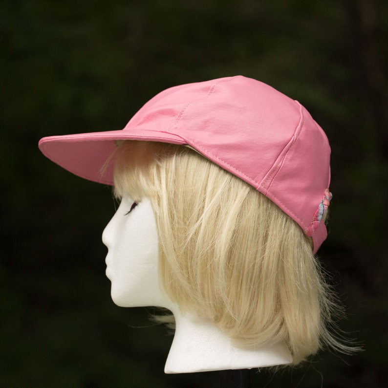 May include: A pink leather baseball cap with a white and blue trim. The cap is on a mannequin with blonde hair.