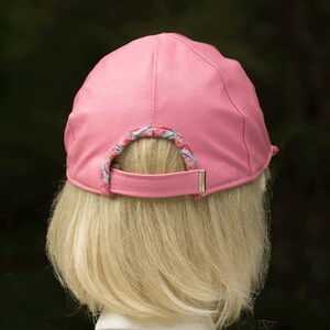 May include: A pink leather baseball cap with a patterned fabric lining around the back opening.
