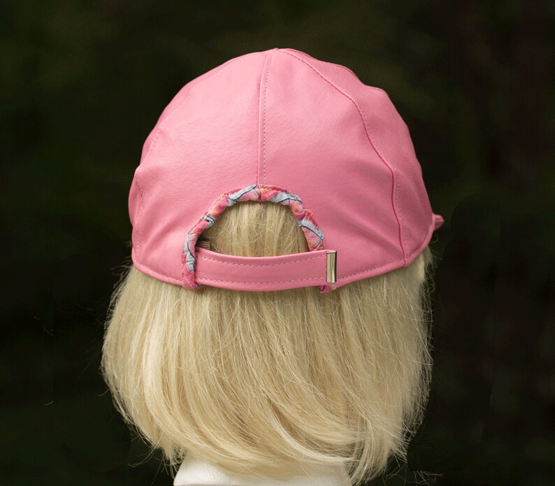 May include: A pink leather baseball cap with a patterned fabric lining around the back opening.