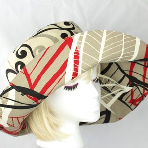 Reversible Summer hat with very wide brim. Abstract print pattern with black, red and white on a beige background. The reverse side has black and grey swirls on a light beige background. Sewn from cotton duck which is slightly waterproof.