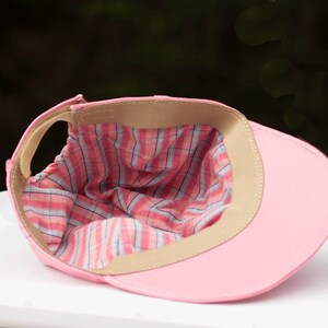 May include: Pink baseball cap with a plaid lining. The cap is turned inside out to show the lining.