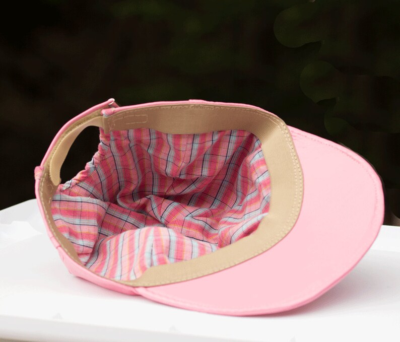 May include: Pink baseball cap with a plaid lining. The cap is turned inside out to show the lining.