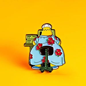 May include: A yellow cartoon character wearing a blue dress with red flowers sits at a desk in front of a computer. The character is facing away from the viewer. The desk is green and has a computer monitor and a keyboard. The character is sitting on a black office chair with a green base.