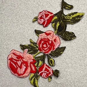 May include: Embroidered patch featuring a cluster of pink and red roses with green leaves. The roses are arranged in a cascading pattern, creating a delicate and romantic design.