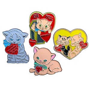 May include: Four enamel pins featuring cats with hearts and romantic sayings. The pins are red, yellow, and blue with white lettering. The sayings on the pins are "Oh Well", "Whatever", "Be Excellent", and "To Each Other".